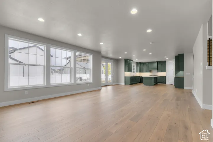 Open-concept living space featuring wood-finish flooring, recessed lighting, large grid-pane windows, and a kitchen equipped with custom-colored cabinetry and a central island