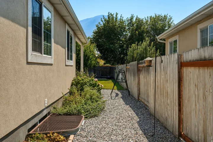 Charming side-yard retreat featuring a gravel pathway lined with mature landscaping, weathered wood privacy fencing, and mountain vistas in the distance