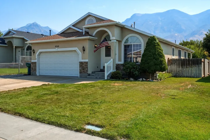 Stucco exterior with stone accents, arched entryway, arched window, attached two-car garage, and established front lawn