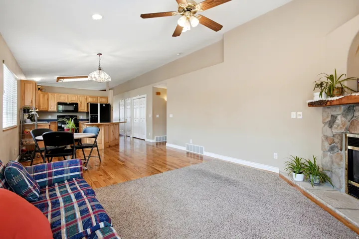 Vaulted ceiling with ceiling fan, stone-surround fireplace, wood-finish flooring, recessed lighting, and wooden cabinetry in the kitchen