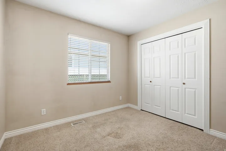 Carpeted flooring, neutral wall paint, white trim, window with blinds, and bi-fold closet doors