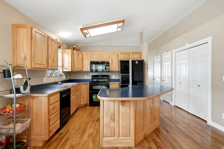 Hardwood flooring, light wood cabinetry, black appliances, kitchen island, and multiple storage closets