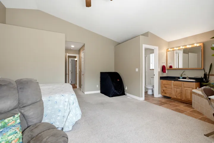 Spacious primary suite with ensuite bathroom featuring wood cabinetry, dual vanity with integrated sink, and large mirror