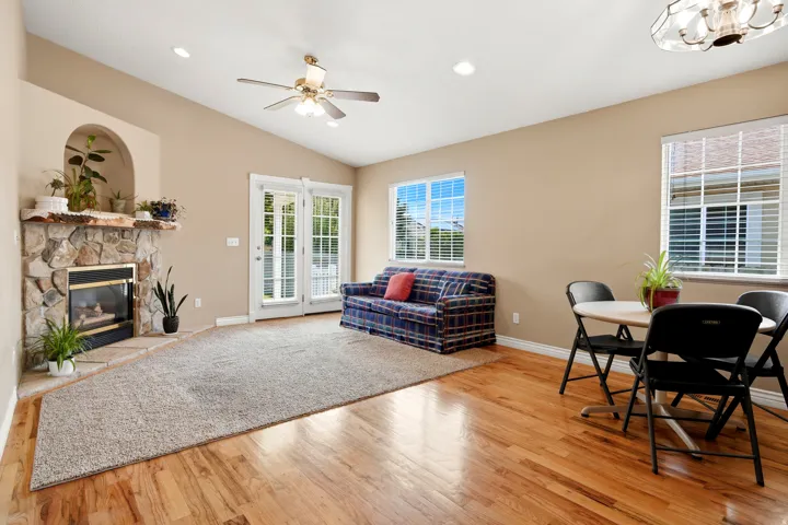 Vaulted ceiling, stone fireplace with mantel, double-paned windows with blinds, wood-finish flooring, and recessed lighting