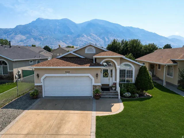 Stucco exterior with stone accents, arched windows, an attached garage, and a manicured lawn