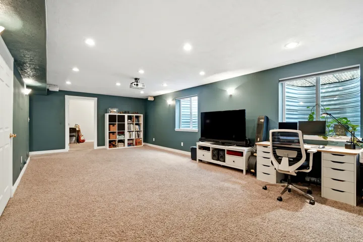 Recessed lighting, large windows with white blinds, neutral carpeting, and a built-in shelf unit
