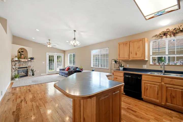 Open-concept kitchen and living area featuring wood-finish flooring throughout, custom wood cabinetry with stainless steel appliances, a large island with rounded edges and metal countertop, multiple windows with plantation shutters providing natural ligh