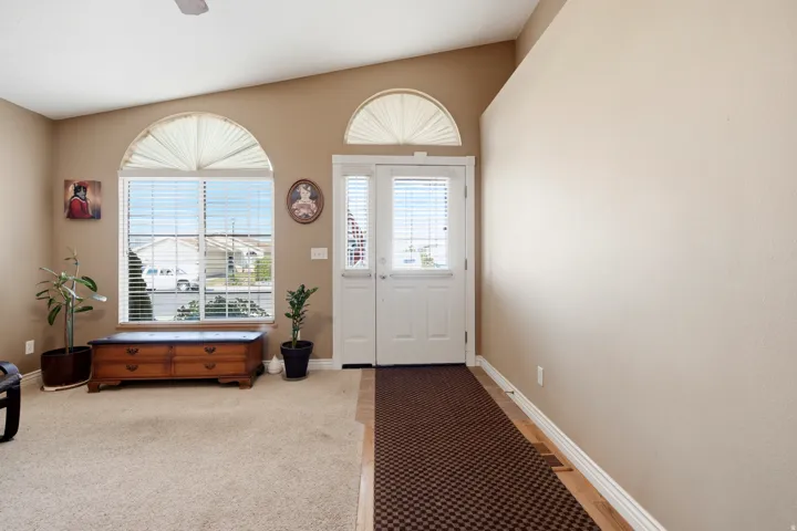Vaulted ceiling with an overhead fan, arched window with horizontal blinds, and a white paneled front door with integrated blinds