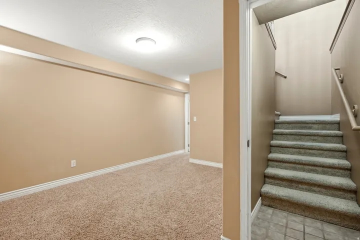 Spacious carpeted recreation room with neutral wall finishes, recessed ceiling lighting, and direct staircase access