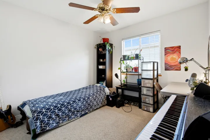 Versatile bedroom featuring neutral carpeting, ceiling fan with integrated lighting, and ample natural light from large window
