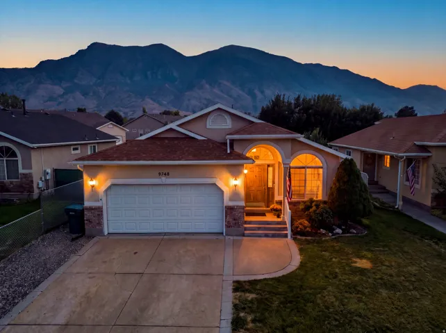 Stucco exterior with stone accents, attached garage, concrete driveway, arched entryways, and a front lawn with established landscaping