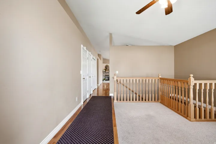 Vaulted ceiling with ceiling fan, wood-finish flooring, light-toned carpeting, and wood balustrade