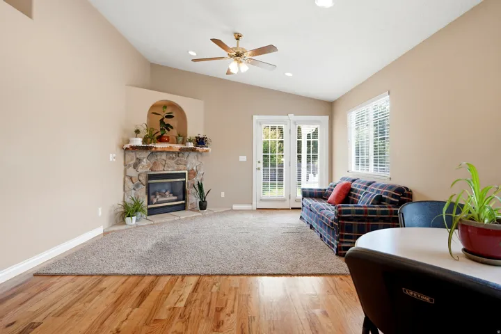 Vaulted ceilings, wood-finish flooring, stone-clad fireplace with mantel, ceiling fan with integrated lighting, and French doors