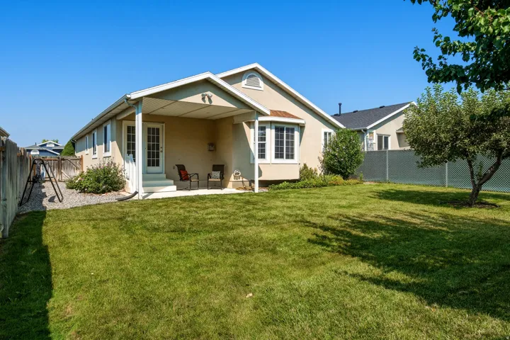 Expansive backyard featuring a lush lawn, covered patio, stucco exterior, and a bay window