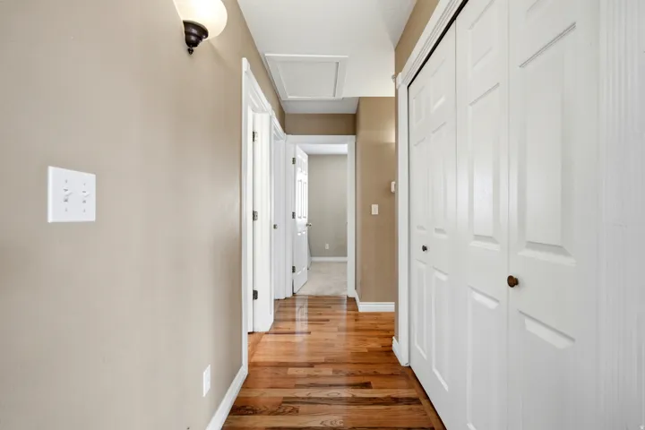 Hallway with warm wood-finish flooring, white six-panel doors, neutral wall finishes, and recessed ceiling lighting throughout