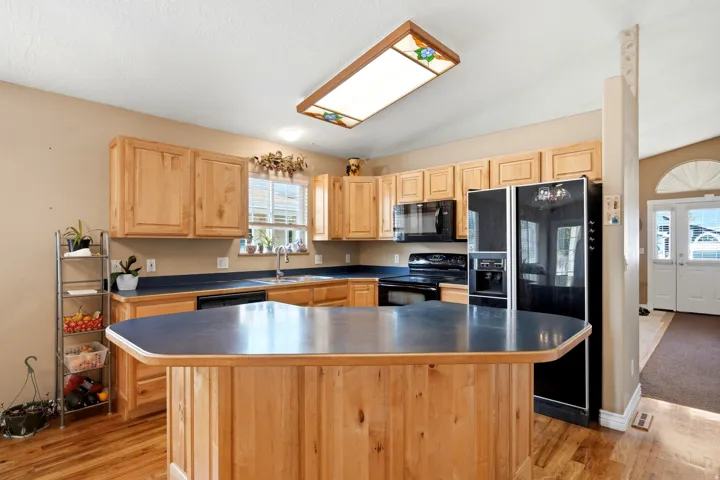 Kitchen featuring wood cabinetry, black appliances, a central island with a dark countertop, and wood-finish flooring