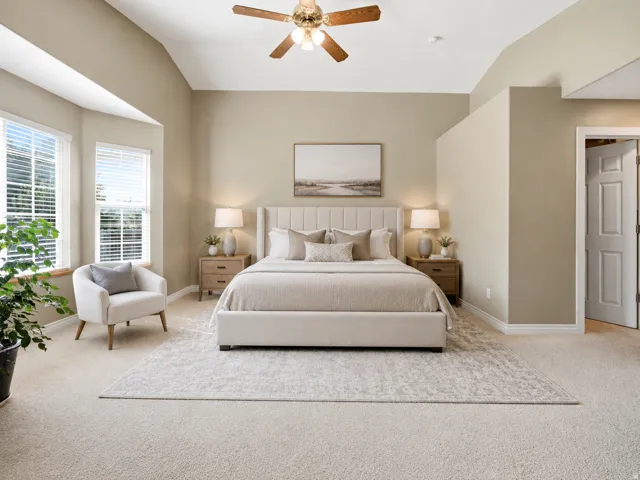 Primary Vaulted ceiling with a ceiling fan, bay window with blinds, light-colored carpet flooring, and a neutral color palette throughout AI staged