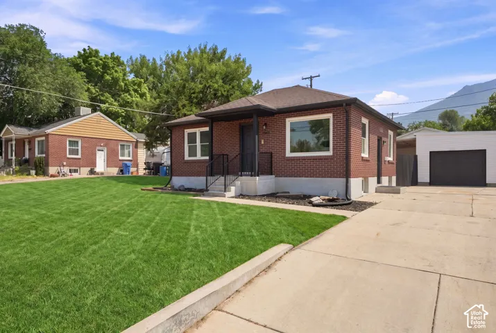 Brick exterior, covered entry, front lawn, concrete driveway, and detached garage