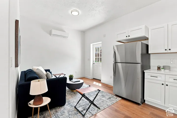 Wood-finish flooring throughout, white shaker-style cabinetry with matte black hardware, stainless steel refrigerator, white countertops, and a white split-unit air conditioning system