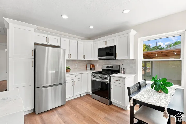 Bright, updated kitchen featuring white cabinetry, stainless steel appliances including a gas range and refrigerator, subway tile backsplash, and wood-finish flooring