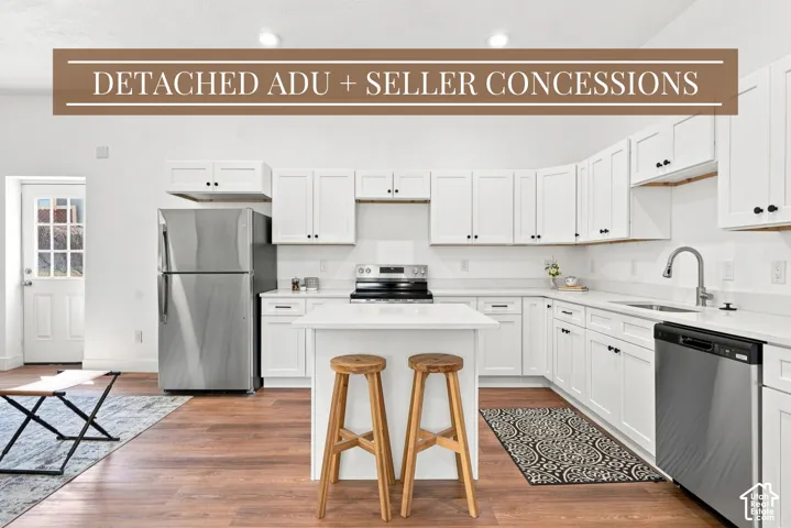 White cabinetry with black hardware, stainless steel appliances, wood-finish flooring, white countertops, and kitchen island with seating