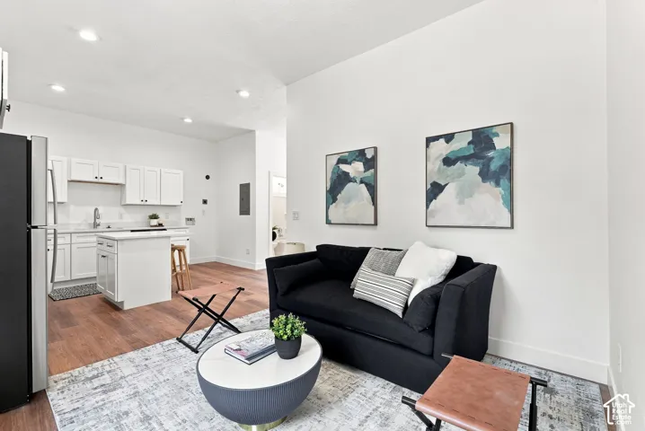 Open-concept living area featuring a black upholstered sofa, white cabinetry throughout the kitchen, stainless steel appliances, wood-finish flooring, and recessed ceiling lighting