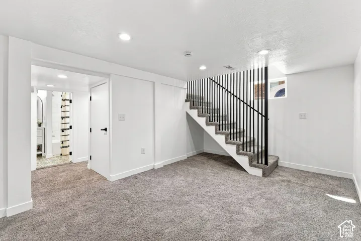 Carpeted flooring, contemporary staircase with black vertical balusters, recessed lighting, white walls, and a separate room with a vanity and bathtub
