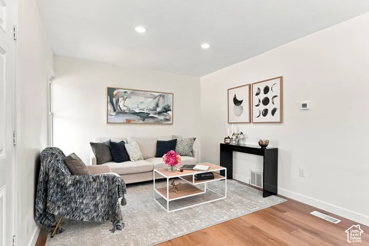 Bright living room featuring recessed ceiling lighting, wood-finish flooring, and a neutral color palette