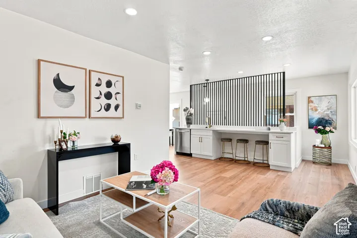 Open-concept living space featuring warm wood-finish flooring, recessed ceiling lighting, and a custom kitchen with white cabinetry, stainless steel appliances, and a black vertical slat range hood