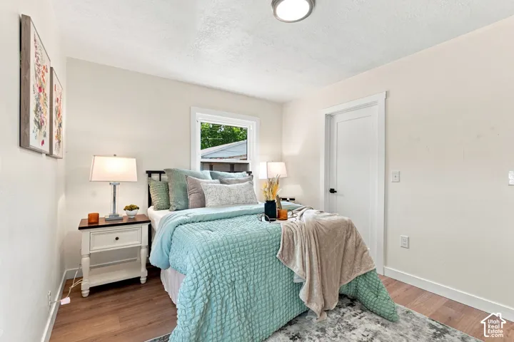 Bright secondary bedroom featuring wood-finish flooring, dual bedside table lamps with fabric shades, a casement window with natural light, and a ceiling-mounted light fixture