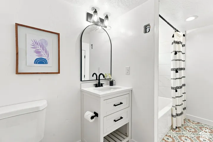 White vanity with black hardware, arched mirror, black faucet, integrated sink, and patterned floor tile