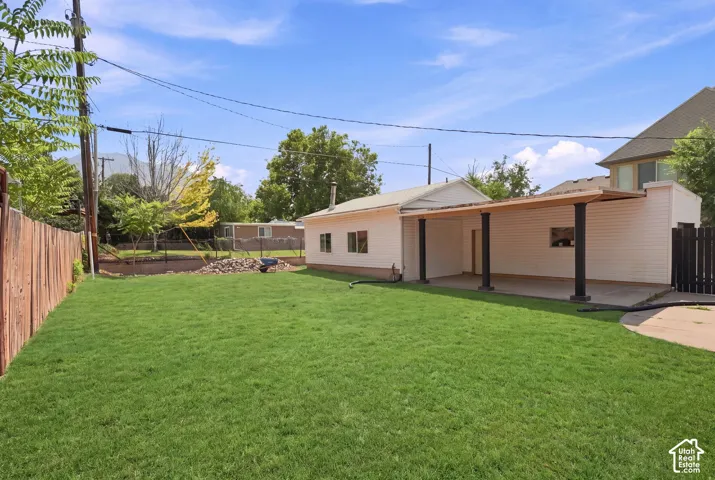 Expansive green lawn with a wood fence, concrete patio, and an extended overhang structure