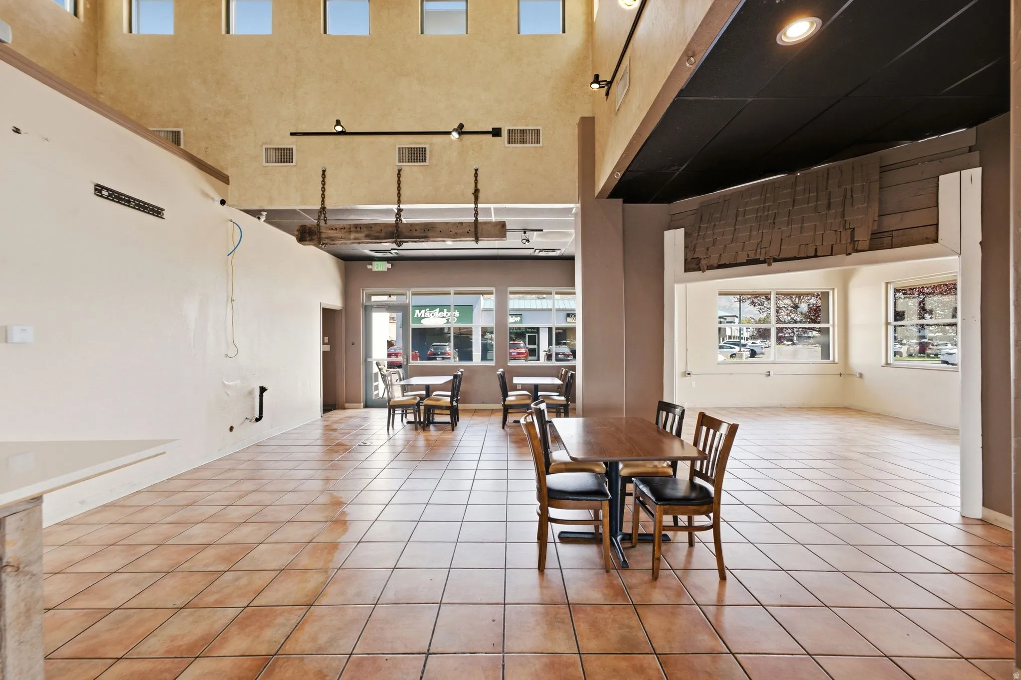 Spacious open-concept commercial or retail space featuring terra cotta tile flooring, soaring ceilings with clerestory windows providing abundant natural light, and large storefront glazing