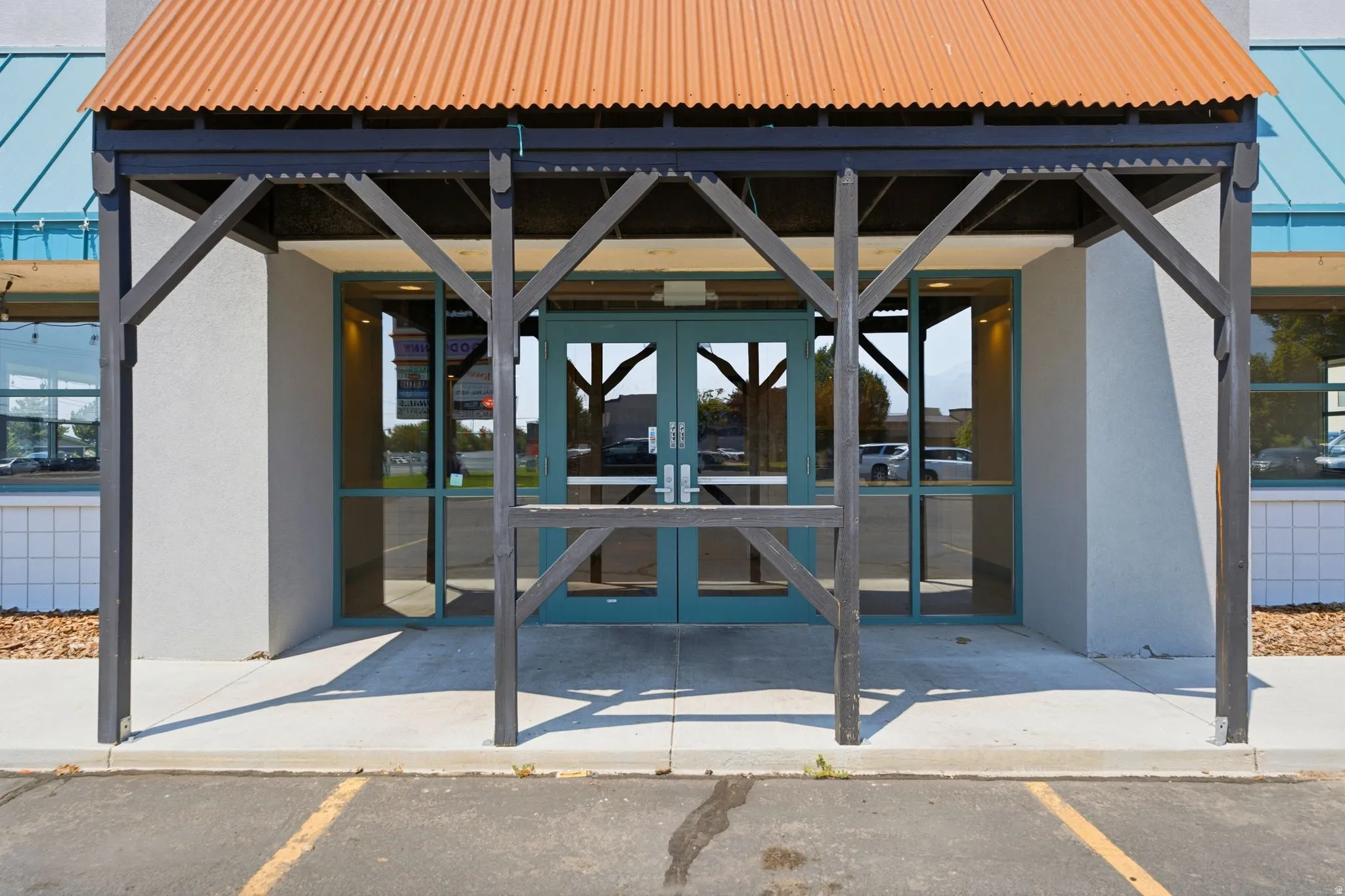 Modern commercial storefront featuring a welcoming covered entry with exposed timber framing, dual glass and metal doors, expansive front glazing for optimal visibility, and a distinctive corrugated metal roof