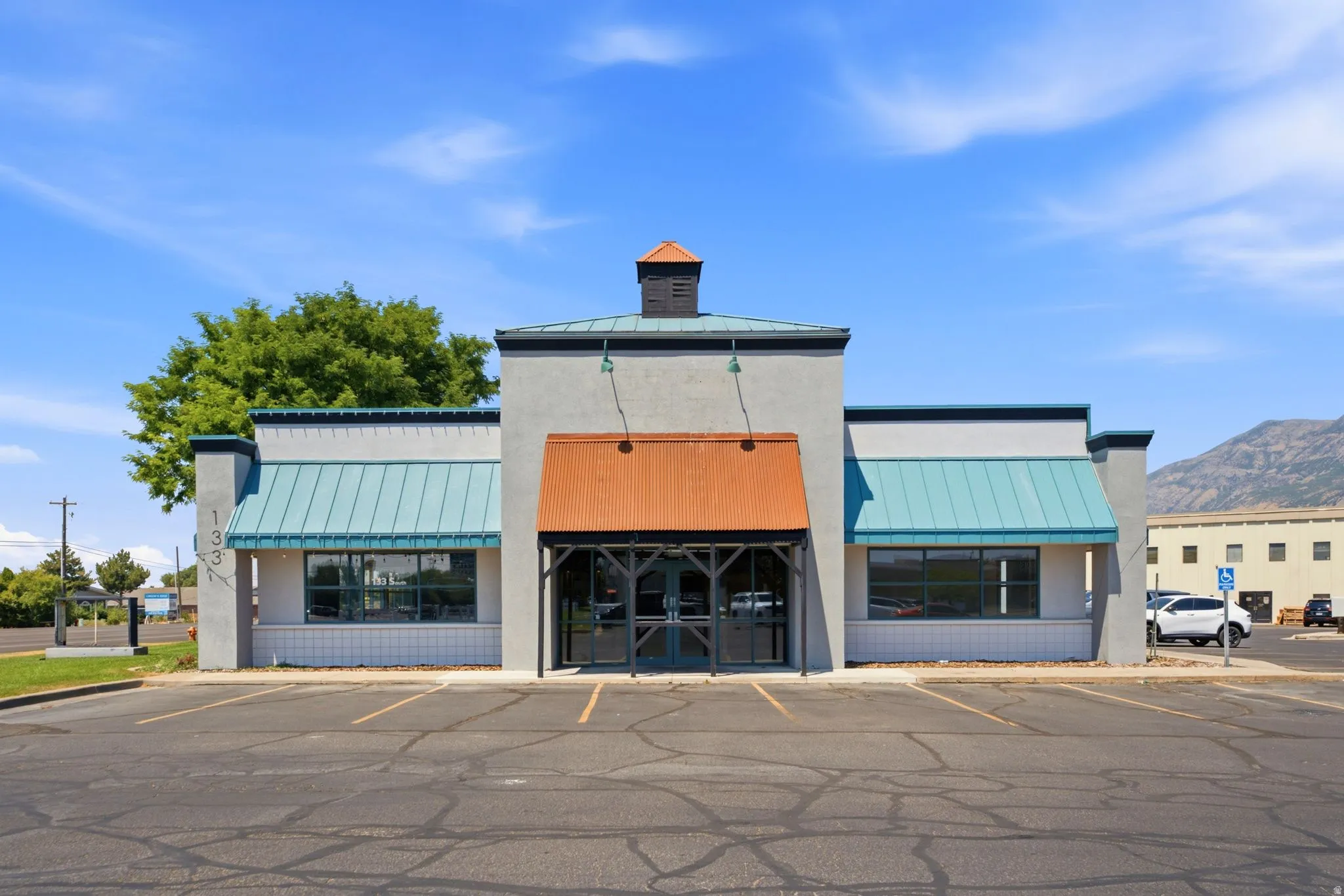 Contemporary commercial storefront featuring a distinctive multi-bay facade with turquoise metal awnings, orange accent paneling, and black trim detailing