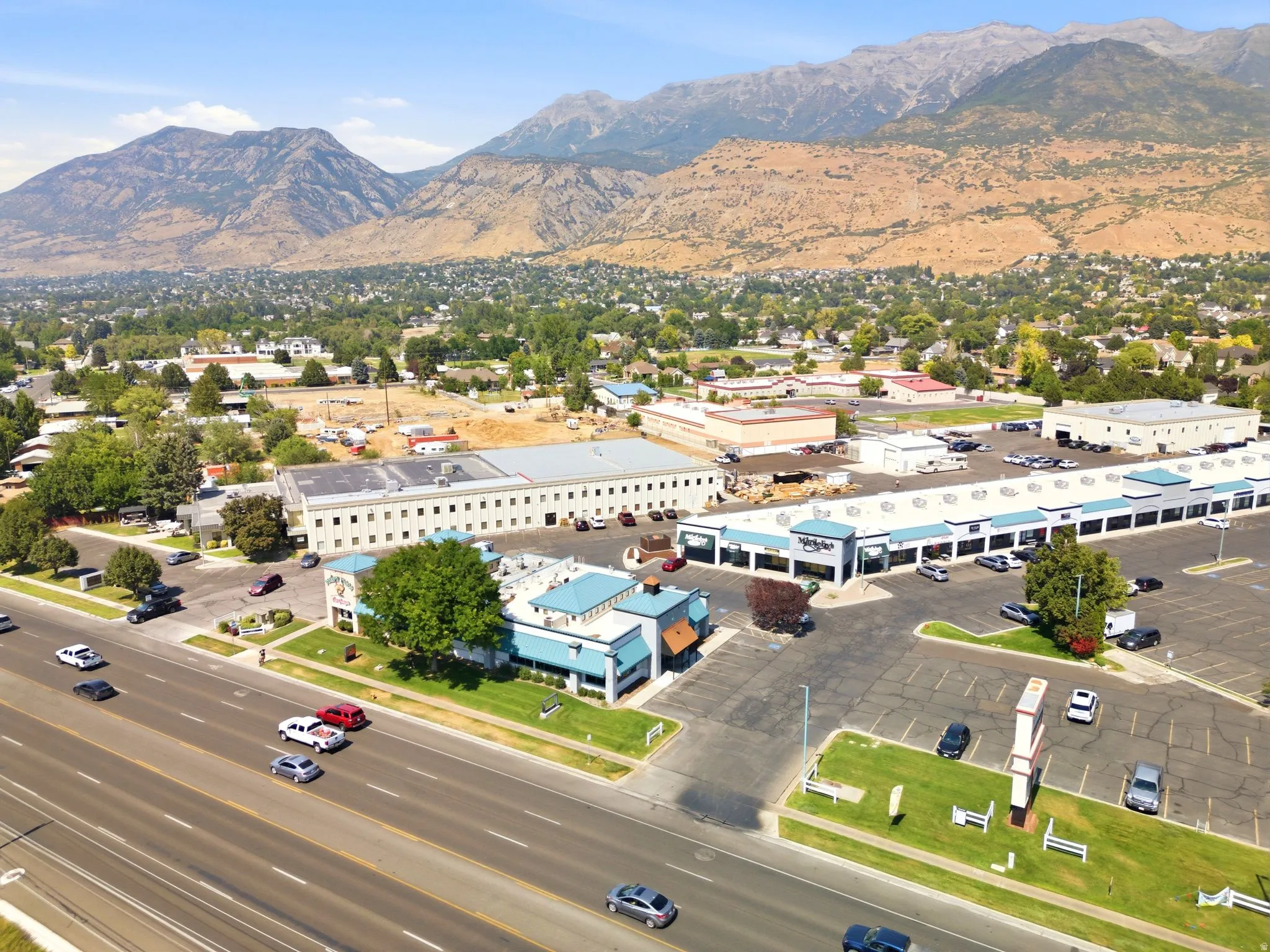 Commercial building with multiple storefronts, ample paved parking, direct road frontage, and prominent street signage