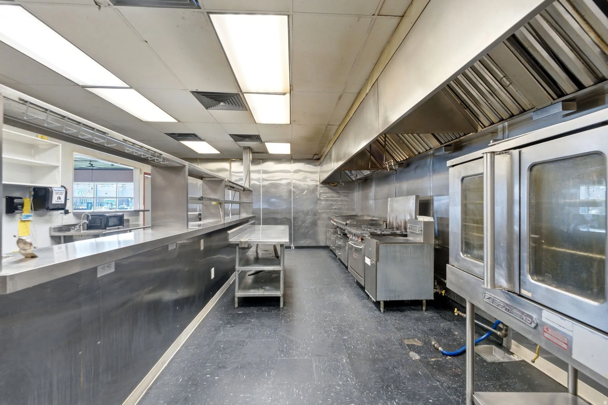 Commercial-grade kitchen featuring extensive stainless steel surfaces, multiple ovens, a large range hood system, and an integrated service counter