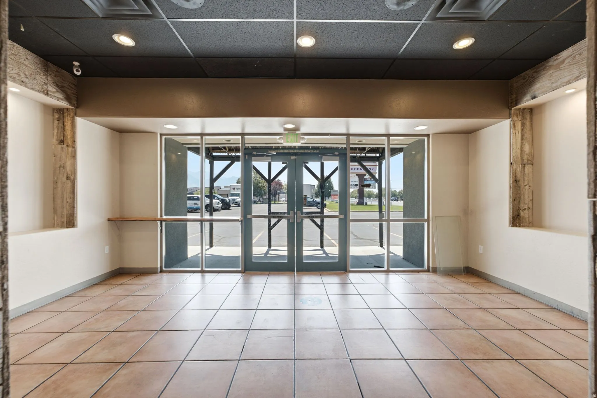 Full-height glass entry doors, recessed lighting, neutral tile flooring, and exposed wood beam accents