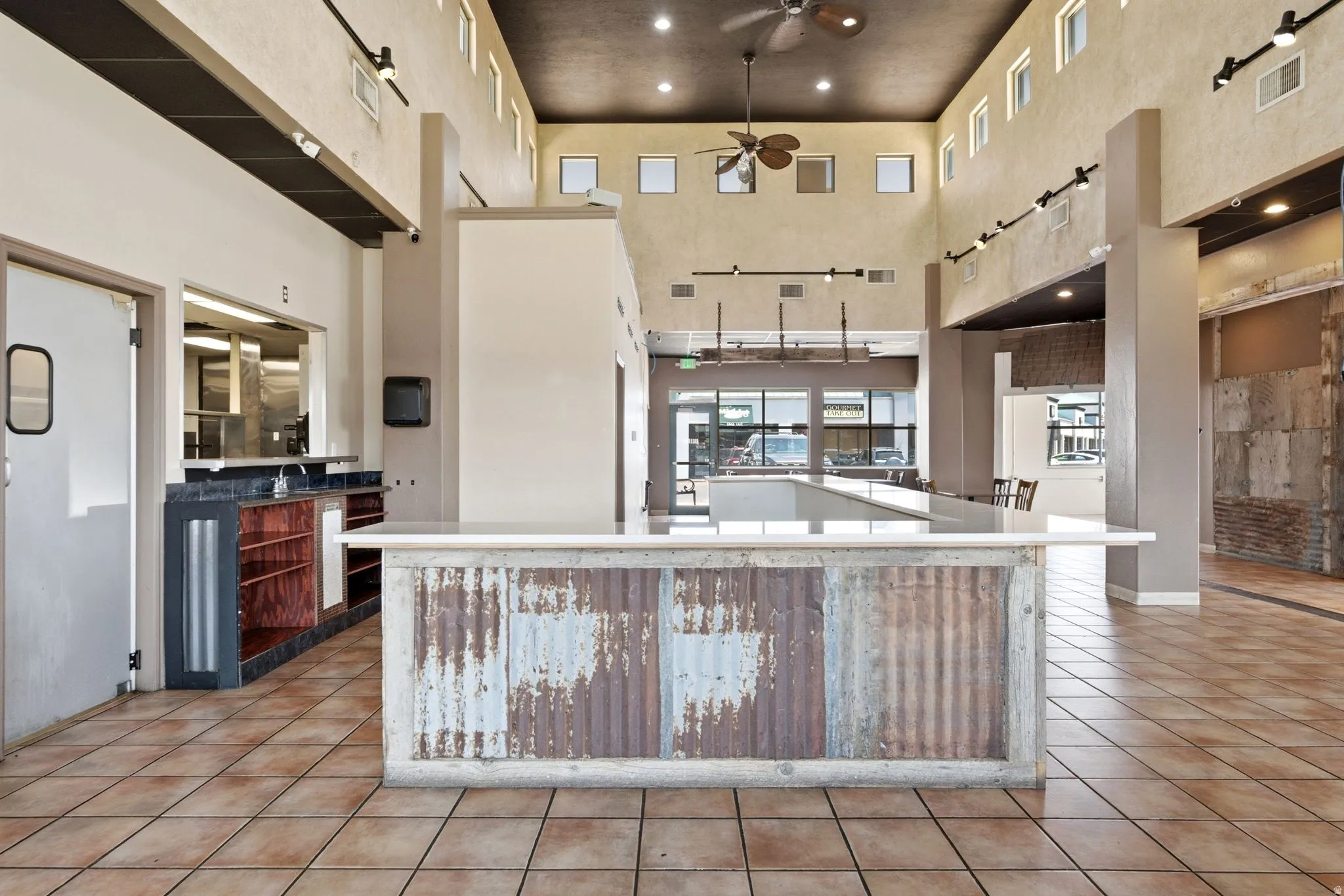 Expansive open-concept kitchen and dining area featuring a large central island with corrugated metal detailing, white quartz countertops, stainless steel appliances, and wood-finish tile flooring throughout