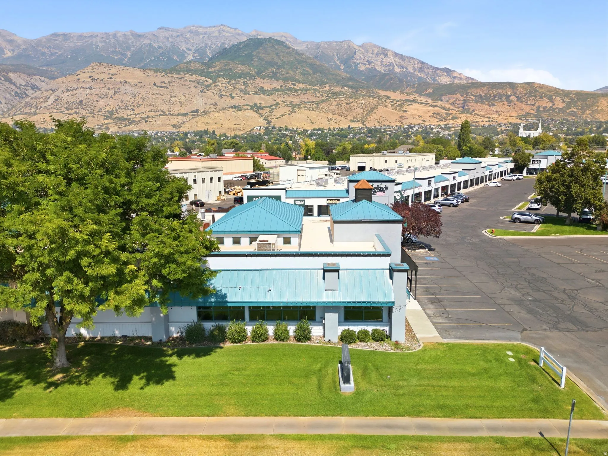 Commercial or mixed-use property featuring a distinctive turquoise metal roof, clean-lined modern architecture, and ample paved parking