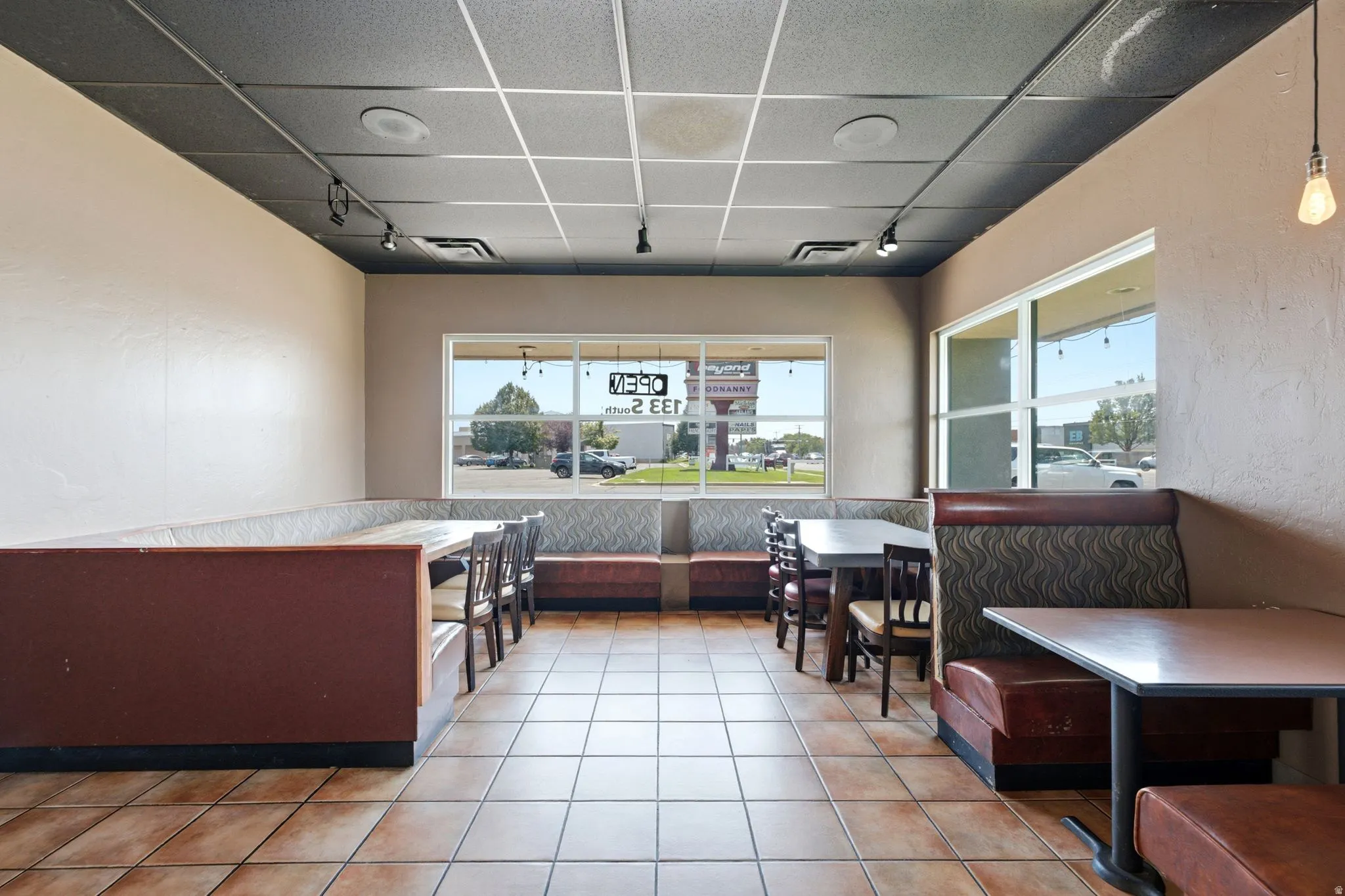 Spacious dining area featuring tile flooring, built-in booth seating with upholstered cushioning, and large front-facing windows providing natural light