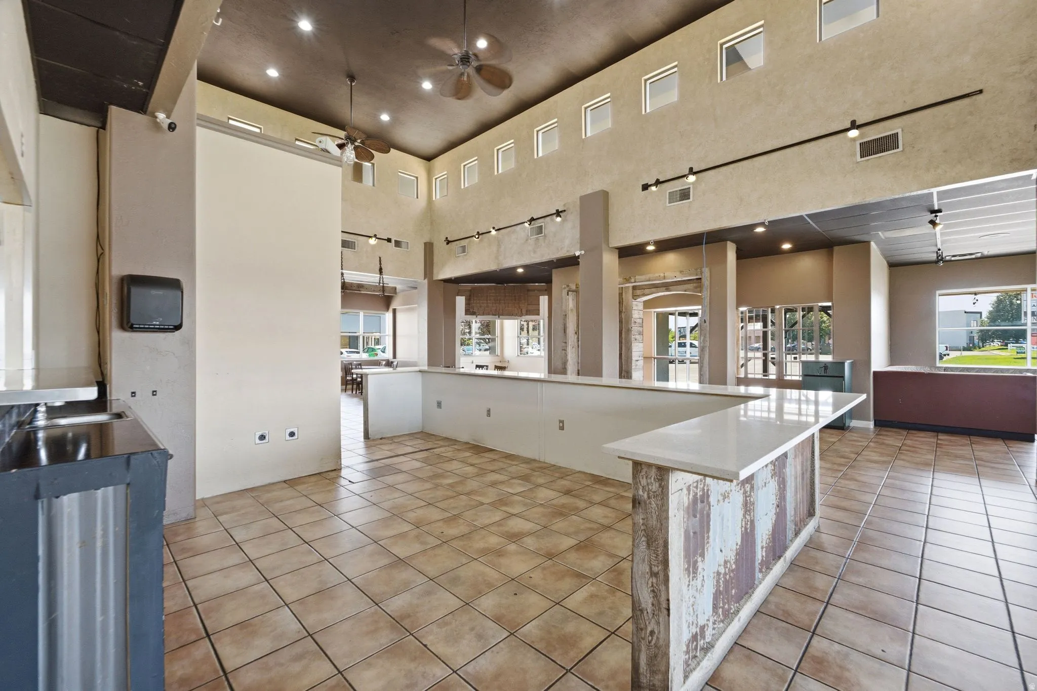 Spacious commercial or retail interior featuring soaring ceilings with recessed lighting, tile flooring throughout, and an open floor plan with multiple service counters