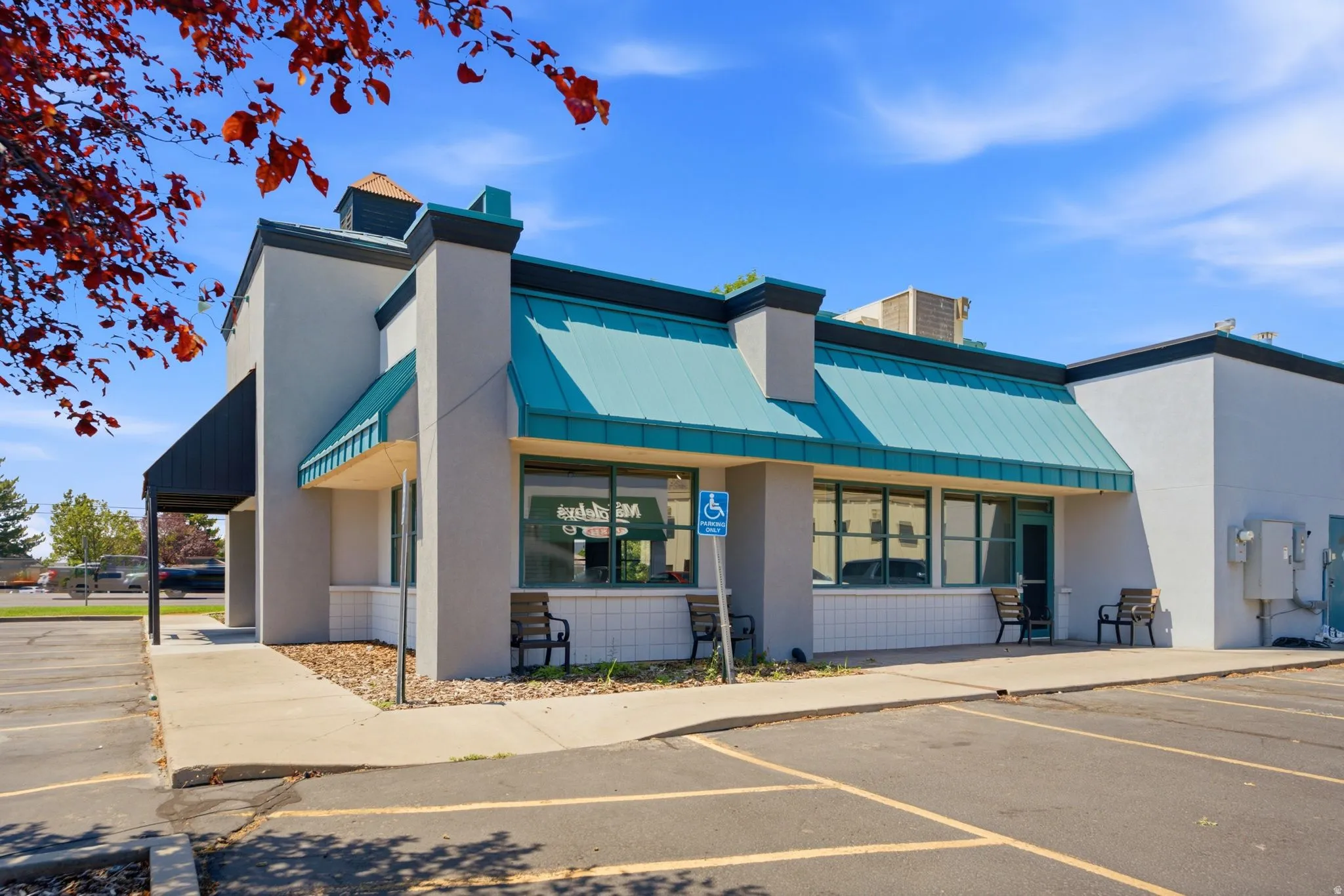 Contemporary commercial storefront featuring a turquoise metal awning, large display windows with visibility from the parking area, gray composite exterior cladding, and a covered entry portico