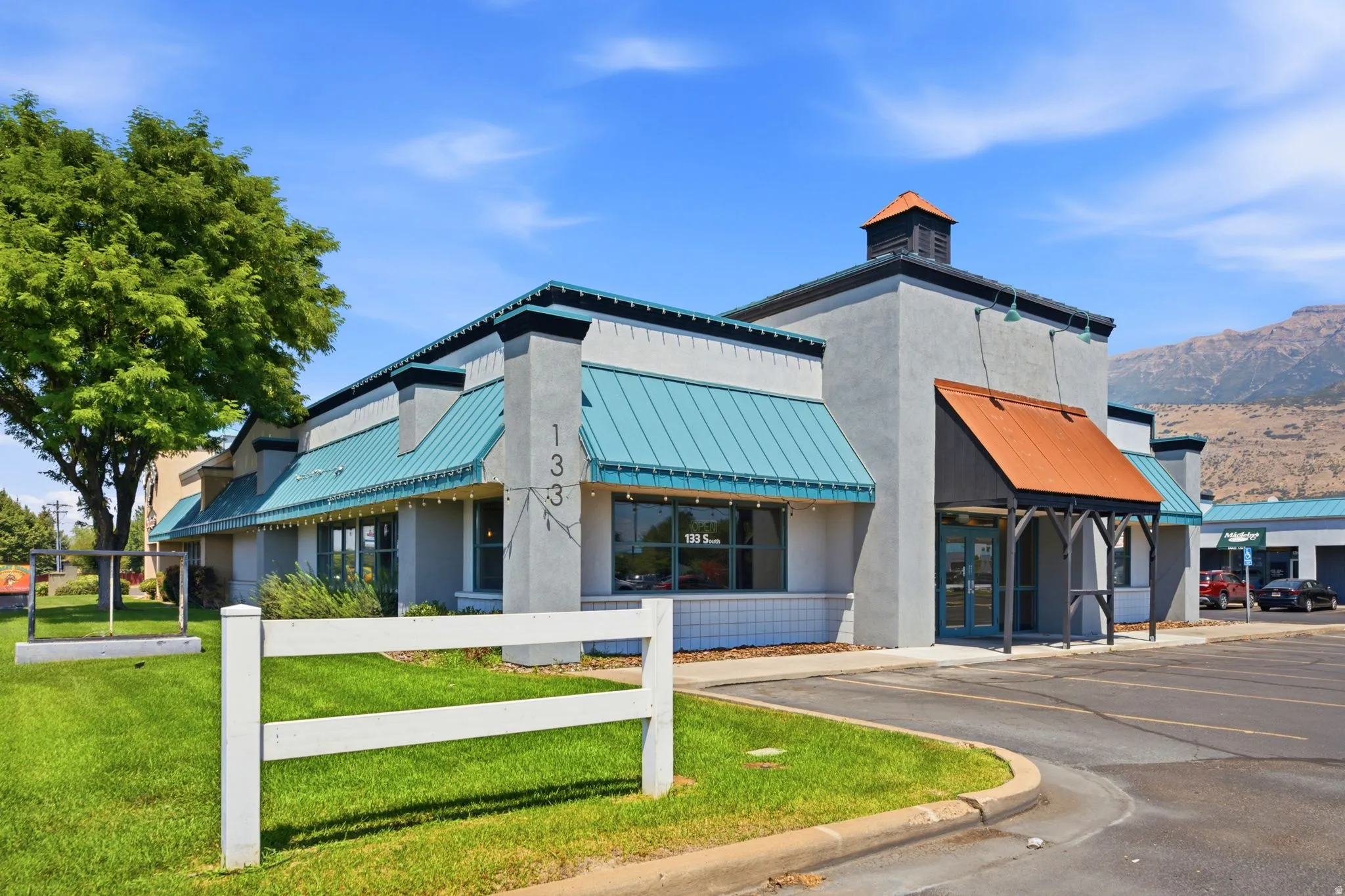 Modern commercial or mixed-use building featuring a striking contemporary design with turquoise and orange metal awnings, clean concrete facade, and cupola-style roof element