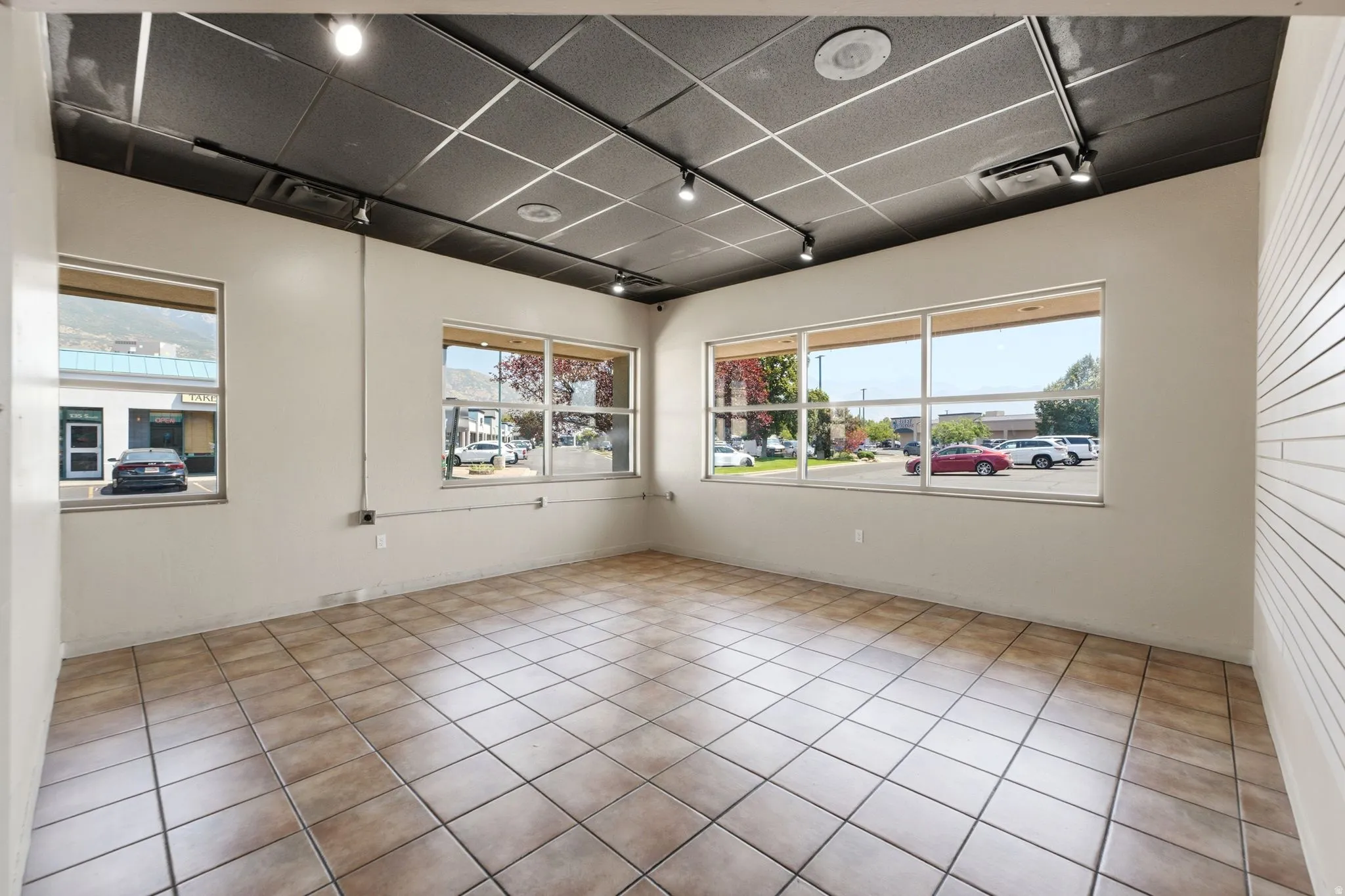 Bright, open retail or office space featuring expansive front-facing windows, tile flooring throughout, recessed ceiling lighting, and ample natural light