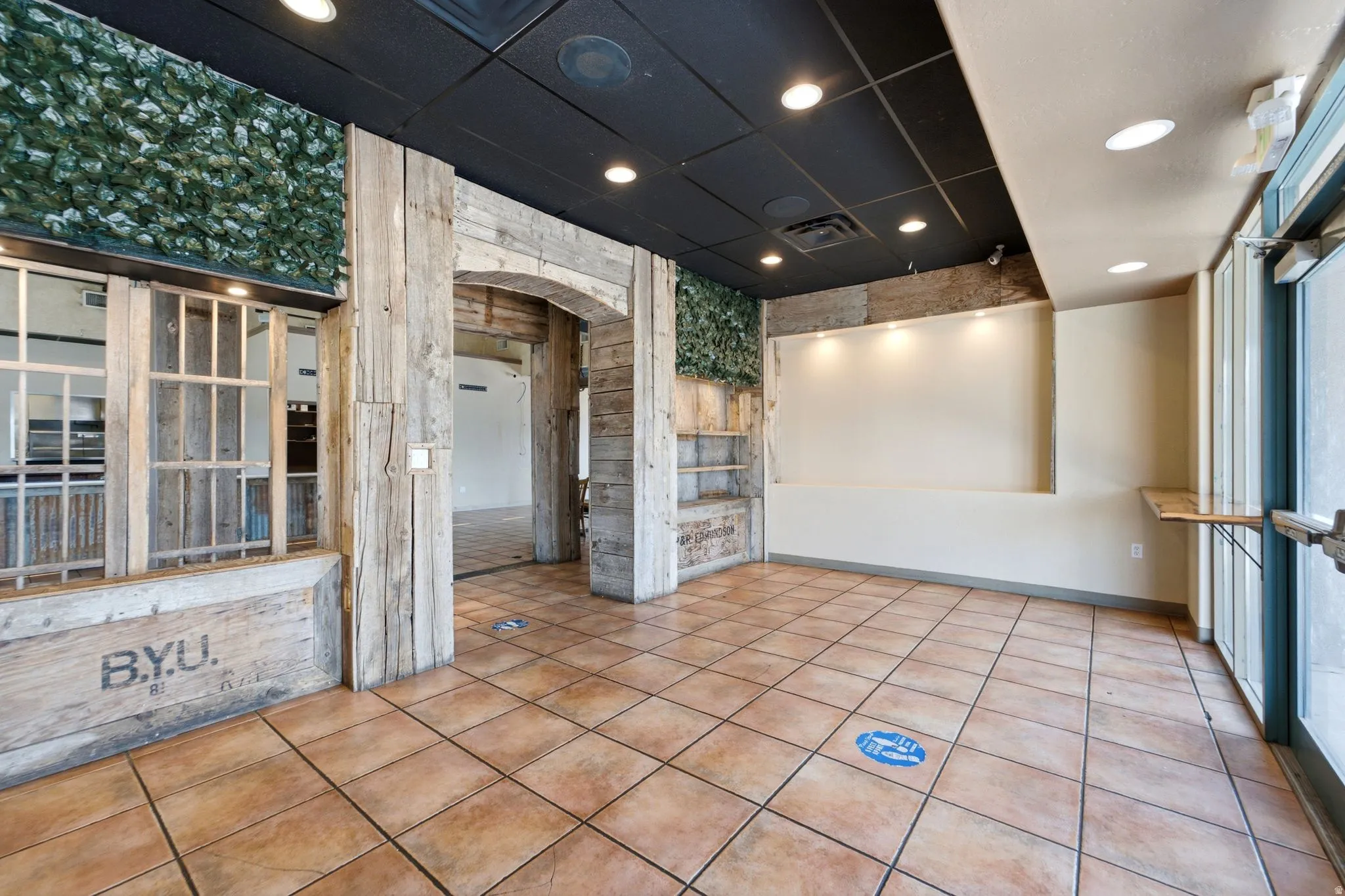 Spacious retail or commercial interior featuring terracotta tile flooring, recessed ceiling lighting, and large front-facing windows with natural light