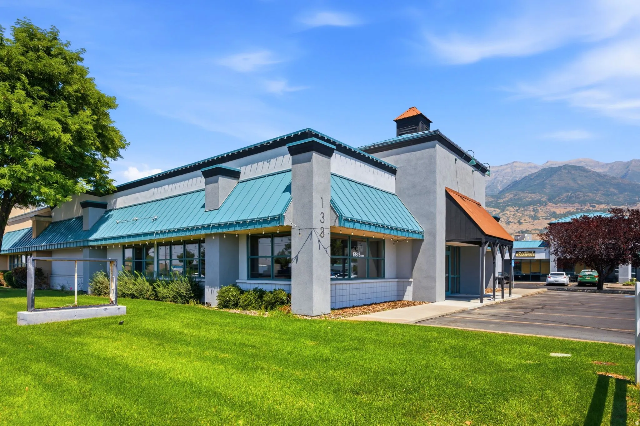 Commercial building with a vibrant teal metal roof, extensive window frontage, and a covered entry