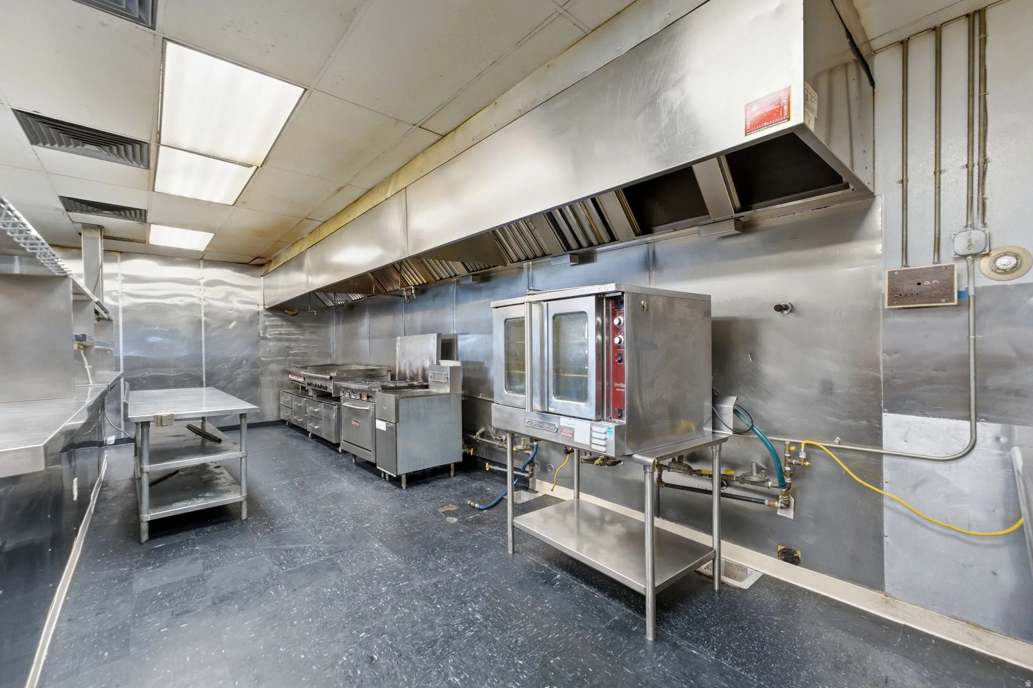 Commercial kitchen featuring stainless steel equipment, expansive exhaust hood system, and durable flooring