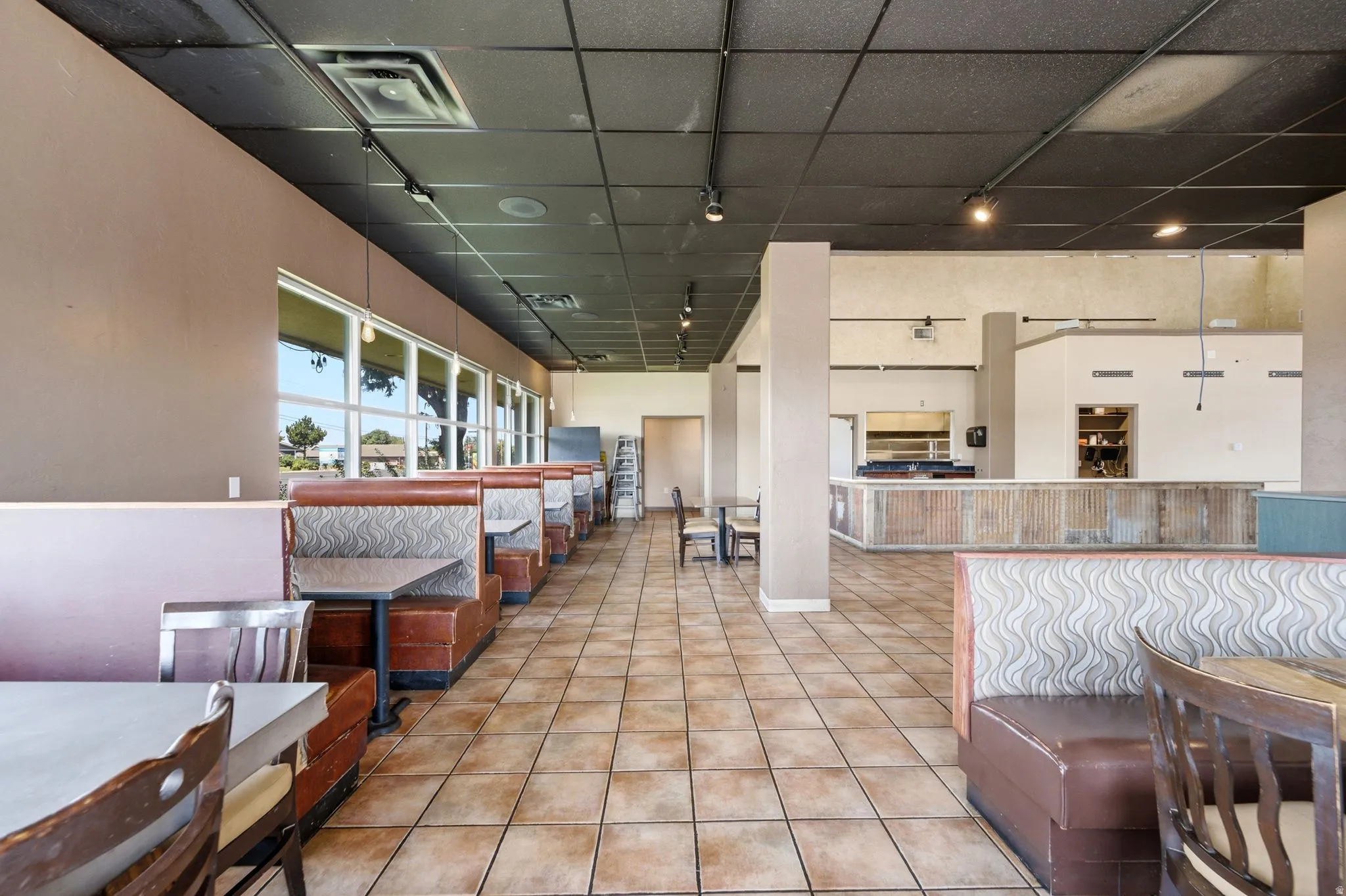 Expansive tile flooring, suspended ceiling with track lighting, multiple large windows, and an integrated counter area