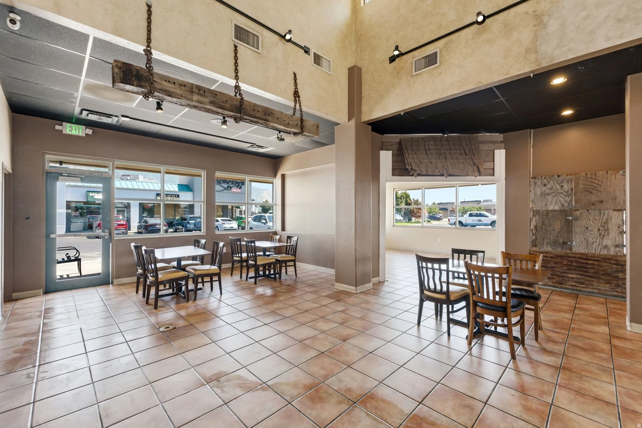 Spacious commercial or multi-use interior featuring polished tile flooring, abundant natural light from expansive storefront windows, exposed ceiling with recessed lighting, and structural support columns